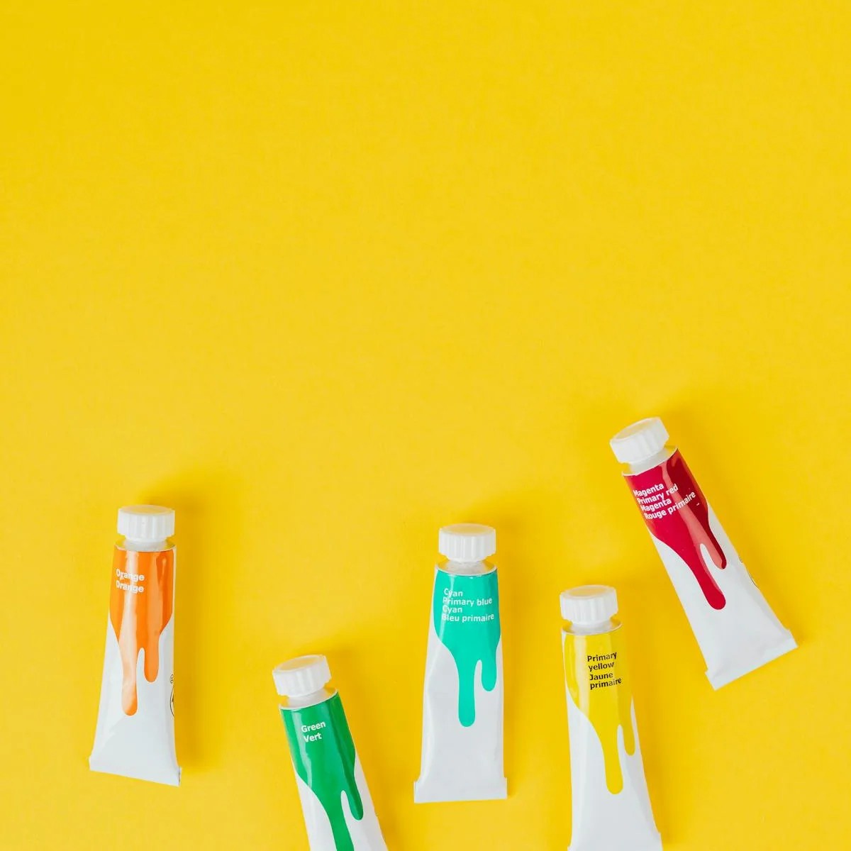 Bright yellow background with four different types of paint tubes