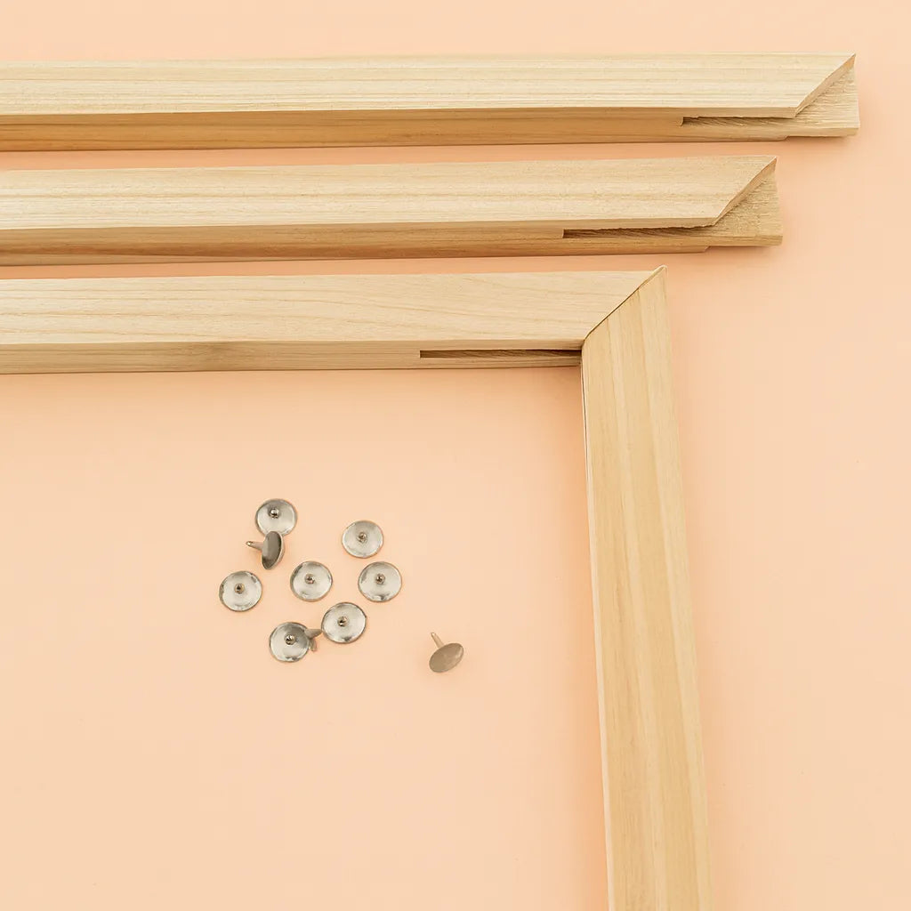 kuvassa kiilakehyksen palaset oranssilla taustalla. Puupalojen keskellää on kasa nastoja.