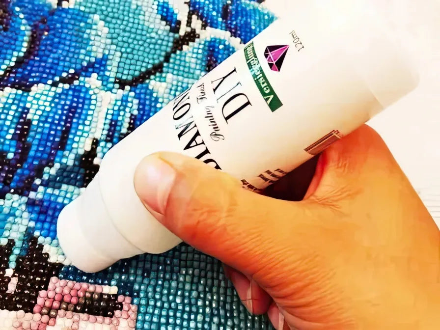 Kädessä timanttimaalaus lakka pullo joka levittää lakkaa valmiin timanttimaalauksen päälle.