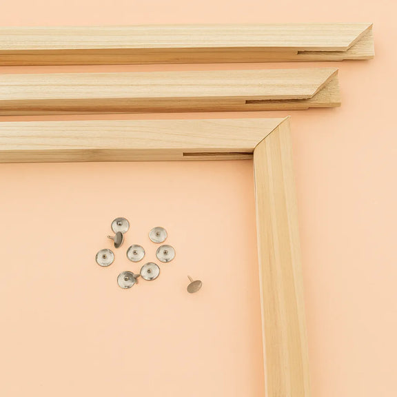 Wooden 40x50 cm paint by numbers stretcher frame before assembly. Four wooden pieces and metallic fastening pins are arranged on a light background, ready for frame assembly.