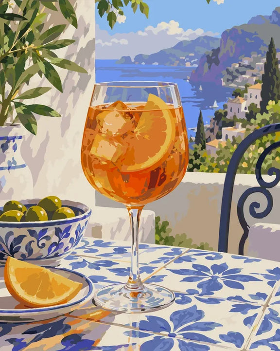 En orange drink med is och oliver i en blåvit skål framför en kust med vita hus