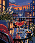 Miniatyrbild: Diamond painting-motiv med en cocktail på ett glasbord med en stad i solnedgången bakom