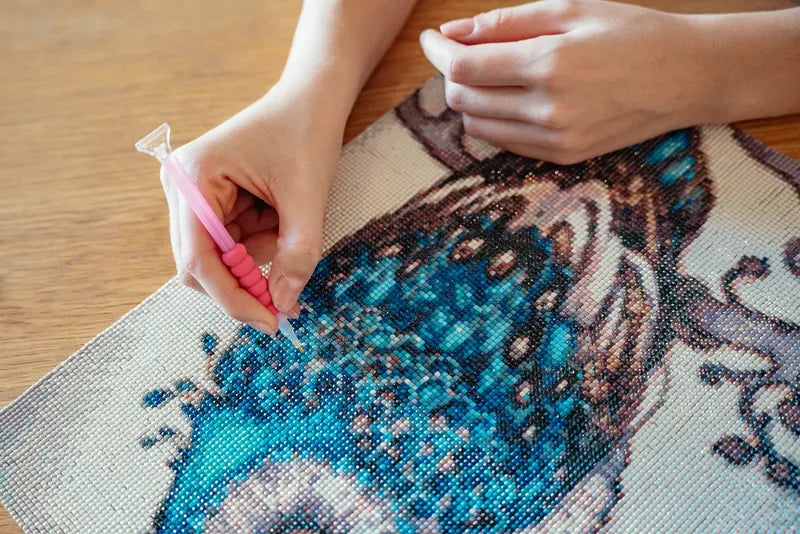 Close-up of diamond painting drills being placed on a butterfly canvas with an applicator pen